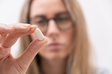 Close up of female hand holding white pill or capsule vitamin supplement close up