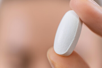 macro photo of hand holding white pill. medical capsule, supplement or antibiotic, pharmaceutical concept