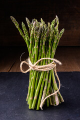 Fresh green asparagus tied with a string on a slate and rustic wooden table 
