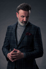 Portrait of a stylish elegant senior businessman with a beard and casual business clothes in photo studio isolated on dark background gesturing with hands
