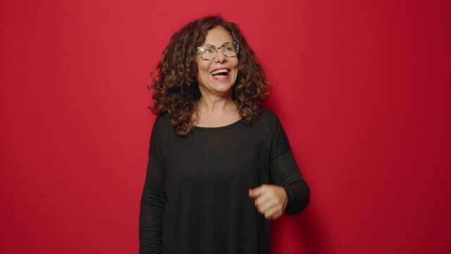 Middle age woman smiling confident pointing with fingers to the side over red background