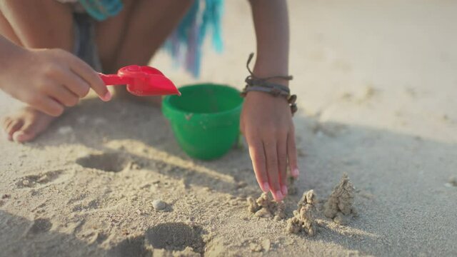 A girl with african braids in a summer costume plays on the beach with shells near the sea with waves under sunny sunset