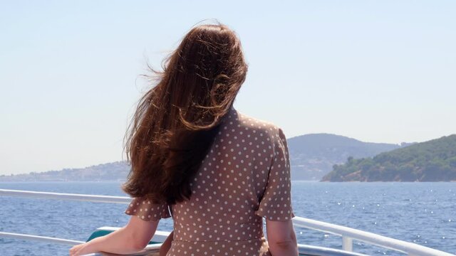 Woman stands at open deck of ferry ship, looking ahead to Princes' Islands. Tourist traveling through the sights of Istanbul on hot summer days. View from back, long hair fly in gusts of wind