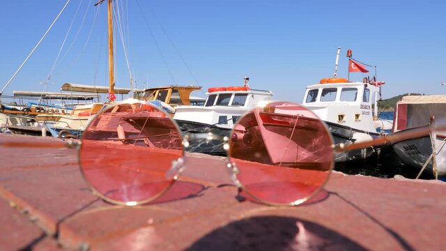 Fishing boats rocking on the water by the pier, view through rose-colored glasses lying on the pavement. Focus in the background, glasses out of focus. Conceptual shot of Burgazada Island, Adalar