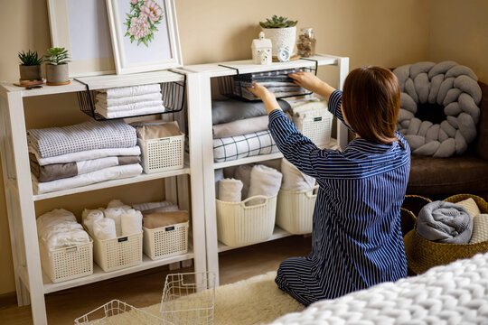 Domestic woman in pajamas neatly putting folded linens into cupboard vertical storage Marie Kondo