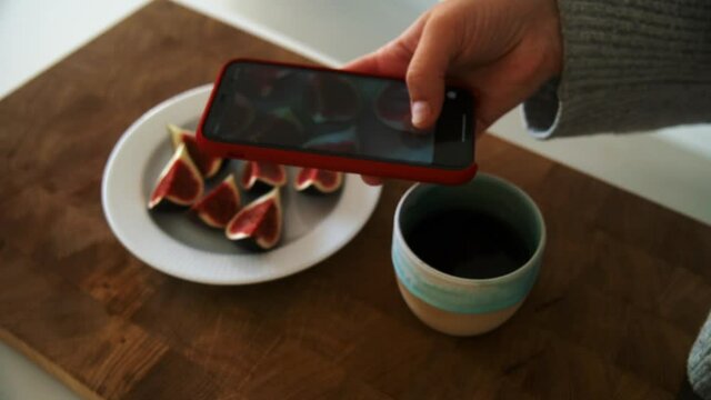 Young woman taking picture of her breakfast. Beautiful ripe cut Figs on a white plate with coffee in the morning zoom in