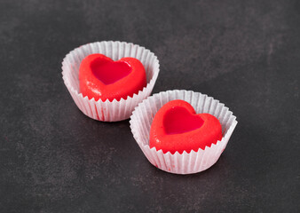 Two Small mousse cake candy in the shape of a red heart with jelly filling in a paper capsule on a dark background. Valentine's Day