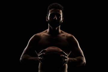 Naklejka na ściany i meble Basketball player holding a ball against black background. Side lit muscular Caucasian man silhouette