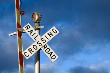 A railroad crossing sign with the barrier in the raised position against moody blue sky.  The evening sunlight highlights the text in the words