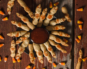Sugar cookies in the shape of Witch Fingers with strawberries jam as blood and almond as fingernails on a red rustic surface with candy corn