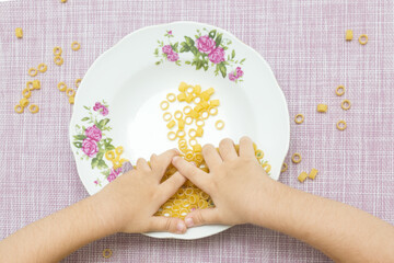 The development of fine motor skills of the hands. Hands of a toddler playing in a plate with pasta. - 480282477