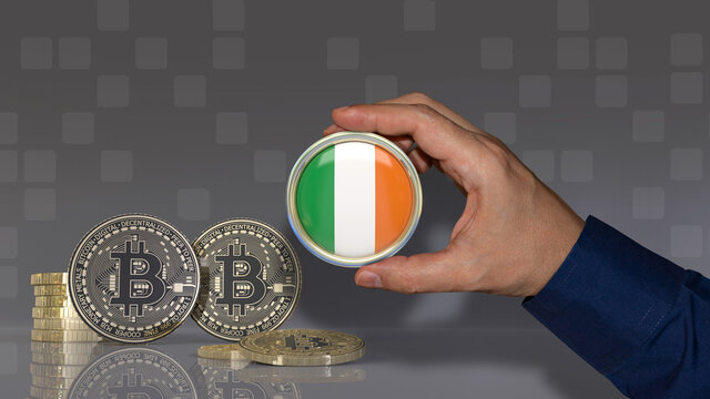 A hand holding a badge with the Irish flag in front of some bitcoins. Crypto currency concept. - Powered by Adobe