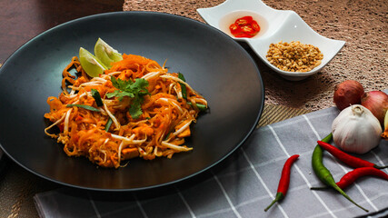 Thai Food Pad Thai (Thai national dish) Pad Thai on black plate with lime and seasonings.