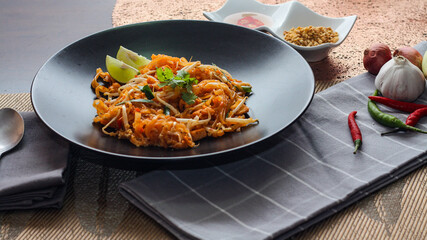 Thai Food Pad Thai (Thai national dish) Pad Thai on black plate with lime and seasonings.