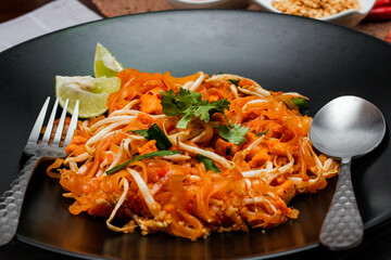 Thai Food Pad Thai (Thai national dish) Pad Thai on black plate with lime and seasonings.