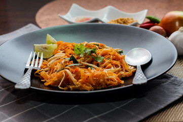 Thai Food Pad Thai (Thai national dish) Pad Thai on black plate with lime and seasonings.