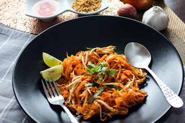 Thai Food Pad Thai (Thai national dish) Pad Thai on black plate with lime and seasonings.