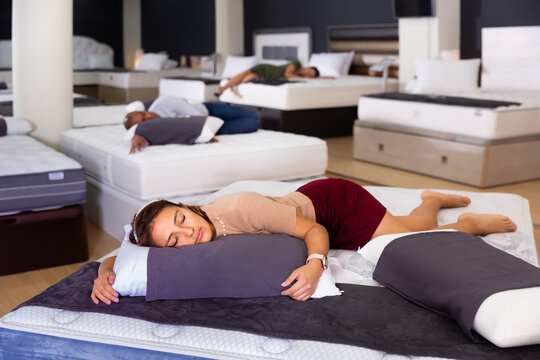Positive latin american woman sleeping on display sample bed with orthopedic mattress in furniture shop