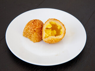 Khanom Kai Hong with sesame or Swan Eggs Dessert, native Thailand fried dessert balls like doughnuts with yellow bean paste on white plate on black wooden background