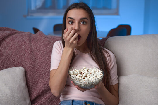 Astonished woman with popcorn watching film at night