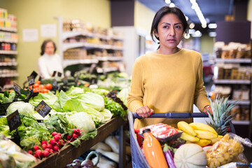 Woman shopping at store, walking among shelves and choosing products