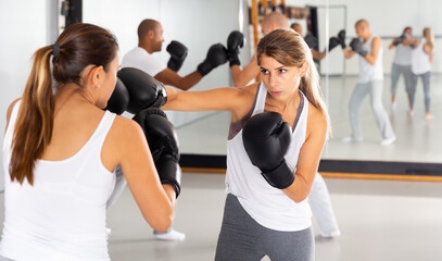 Young woman mastering self defense techniques, practicing punches at boxing gym