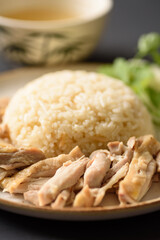 Hainanese chicken rice with coriander, cucumber and chicken soup on black background. Local food in East and Southeast Asia