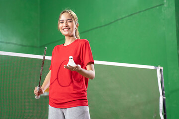 Smiling female badminton player holding racket and shuttlecock - obrazy, fototapety, plakaty