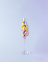 A tall glass glass with multicolored marshmallows on a purple background. The concept of parties.
