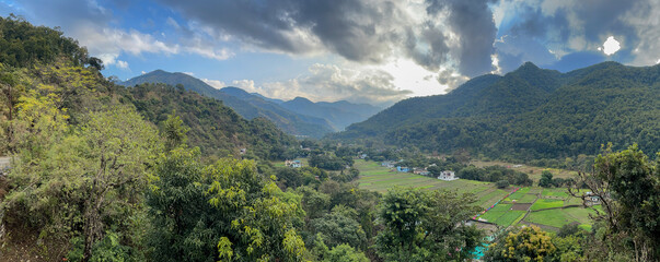 A panoramic view of mountain landscape with fields in the valley and trees all around on the hills