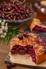 Tall cherry pie stuffed with cherry berries with intertwined ferkh lying on a board on a wooden background