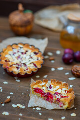 Sandy plum tarts with frangipan and almond petals on a wooden background decorated with plums, one cake is cut and the other is on the background.