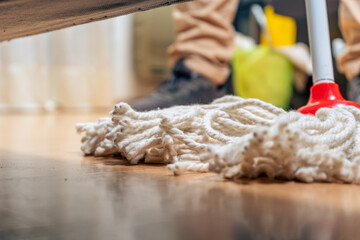 normal view from below of an armchair of a rope mop being wiped across the floor of a house. Cleaning work.