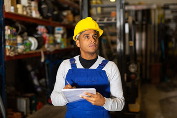 Latin American male warehouse worker making notes while performing inventory of building materials