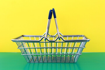 A miniature shopping cart for a supermarket stands empty on a green and yellow background.