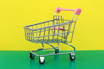 A miniature shopping cart stands on a green and yellow background.