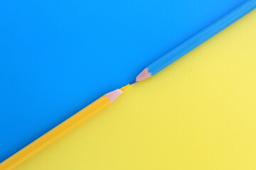 On a blue and yellow background, two pencils of the same color lie at the same time with space for text.
