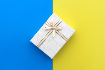 A white gift box stands on the border of yellow and blue.
