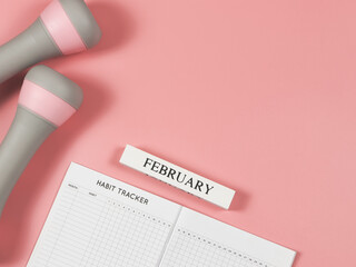 flat lay of habit tracker book, wooden calendar Fabruaty,  gray pink dumbbells on pink background...