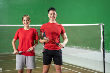 Two smiling badminton players holding rackets standing against net background