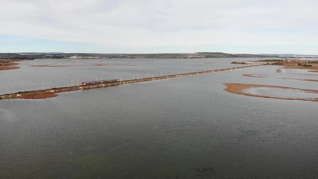 Aerial: passenger train on a dam by the sea in southern France during winter