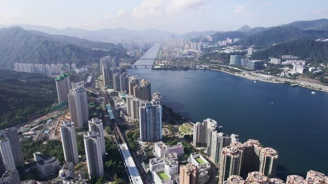 High skyscrapers between the mountains of Lion rock country park and Shing mun river on a cloudy sunny day. Wide angle drone lifting shot