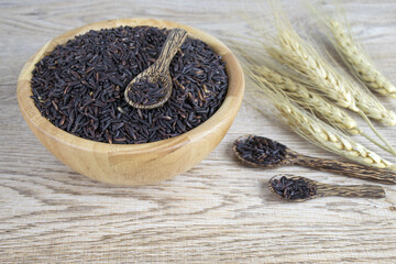 Rice berry in wooden bowl and decorated by dry wheat on wooden table background.