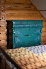 Ancient antique chest of drawers with carved ornaments renovated and painted turquoise located by wall, ready for eco-friendly re-use in wooden country house. Environmental friendliness. 
