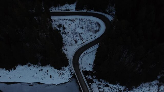 Aerial drone view of a "?" shaped winding road out of the forest across bridge over water