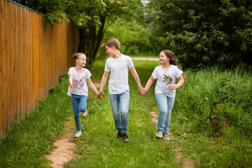 Fototapeta premium Cute little kids are running together on the road. Two sisters and a brother are holding hands, they are having fun, they are happy. The concept of childhood and friendship.