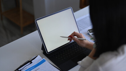 Over shoulder view female accountant holding stylus pen and writing on screen of computer tablet.