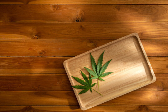 Photo of cannabis leaves in a wooden tray on a wooden table with warm light and shadow background. Copy space Decoration for backdrop artwork design or Banner. Eatable vegetable nature concept ideas