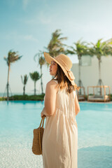 Young Asian woman relaxing beside the pool at luxury hotel. travel and summer concept background.	