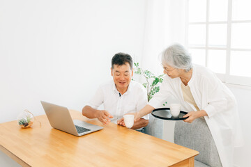 パソコンを使う高齢者男性とお茶を運ぶ女性 